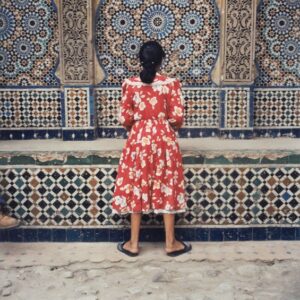Artwork 'Girl in Red - Playing Jacks - Tangier' (1999) by Yto Barrada, showing a girl in a red floral dress playing jacks with her back to the camera against a Moroccan mosaic wall.
